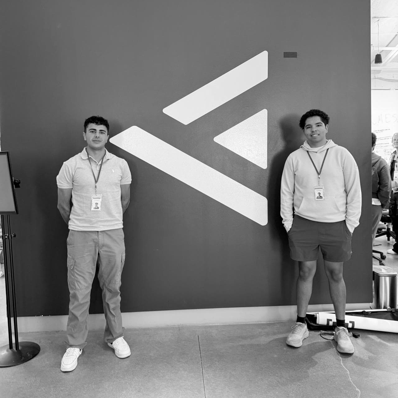Alex Battikha and Nicolas Dos Santos standing in front of a logo wall: Alex on the left in a grey polo, Nicolas on the right in a cream hoodie.